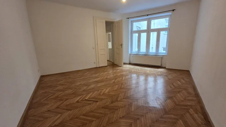 Helles Zimmer mit Fischgrätparkettboden und großen Fenstern, bereit zur individuellen Gestaltung.