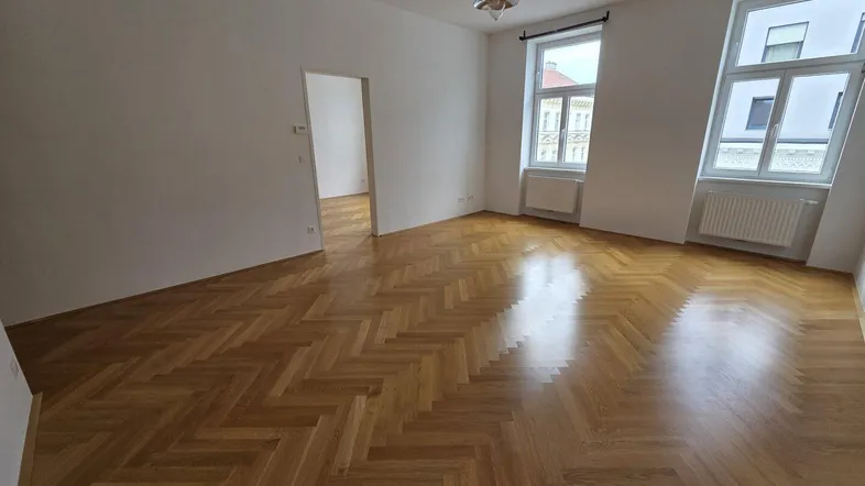 Helles Zimmer mit Fischgrätparkettboden und hohen Fenstern, bereit zur individuellen Gestaltung.