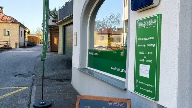 Außenansicht eines Gebäudes mit einem Diner-Schild, einer Geschwindigkeitsbegrenzung und einem Werbeaufsteller auf dem Bürgersteig.