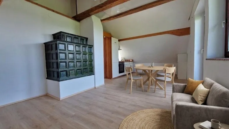 Gemütlicher offener Wohn- und Essbereich mit traditionellem Kachelofen und sichtbaren Holzbalken.