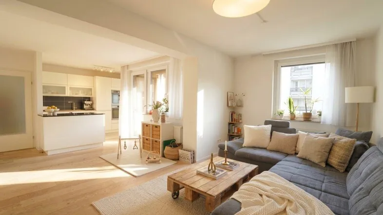 Helles Wohnzimmer mit offener Küche, Holzboden und modernem Sofa, durchflutet von Sonnenlicht.