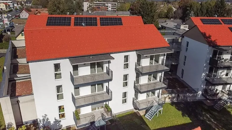 Luftaufnahme von modernen Wohngebäuden mit roten Dächern und Solaranlagen in grüner Umgebung.