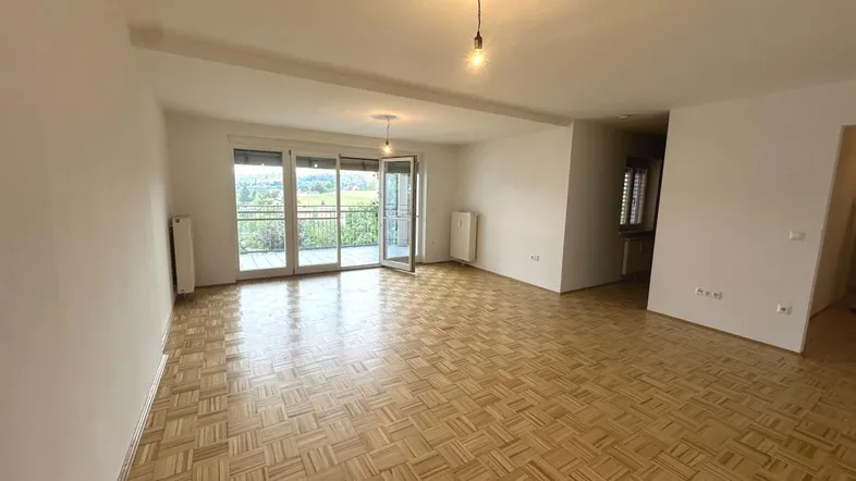 Geräumiges Wohnzimmer mit Parkettboden und Zugang zu einem Balkon mit Weitblick.