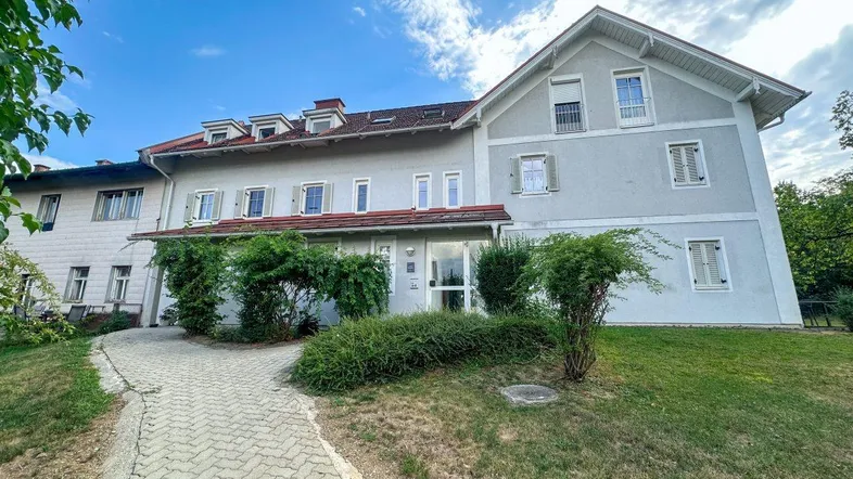 Großes Wohngebäude mit mehreren Fenstern, Dachgauben und einem gepflasterten Zugangsweg.