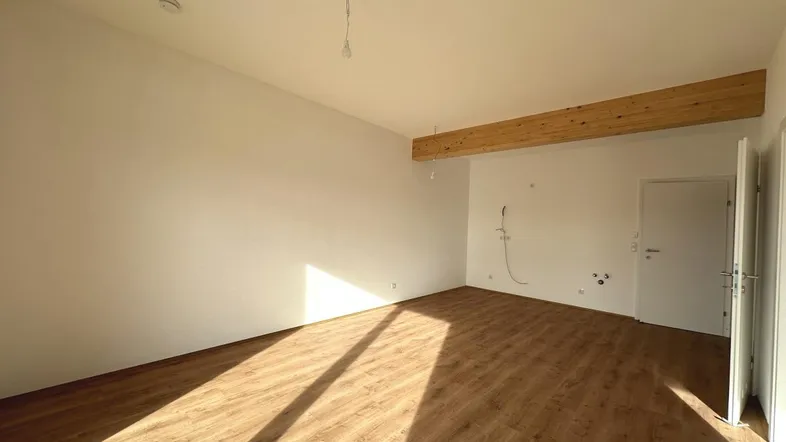 Heller, leerer Raum mit Holzbalken und Laminatboden, durchflutet von Sonnenlicht.