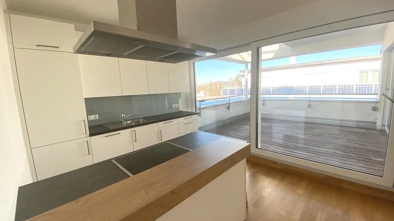 Moderne Küche mit weißen Schränken, Kochinsel und Zugang zu einem sonnigen Balkon.