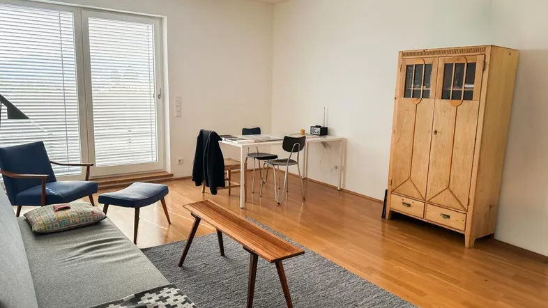 Helles Wohn- und Esszimmer mit Holzboden, bequemer Couch und Zugang zu einem Balkon.