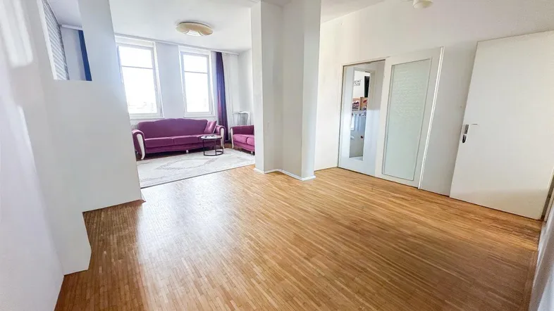 Helles Wohnzimmer mit Parkettboden, weißen Wänden und gemütlichen lila Sofas.
