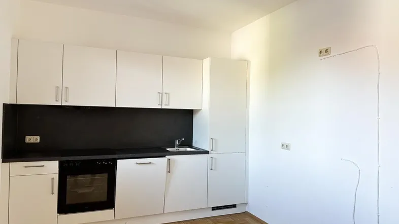 Moderne Küchenzeile mit weißen Schränken, schwarzer Arbeitsplatte und integriertem Backofen.
