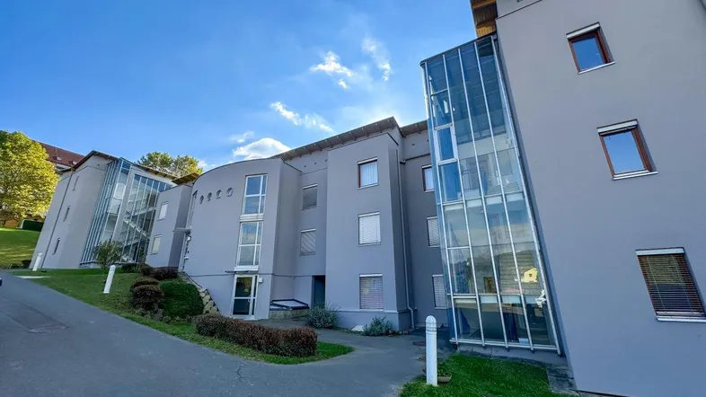 Modernes Mehrfamilienhaus mit grauer Fassade und großen Glasfronten für das Treppenhaus.