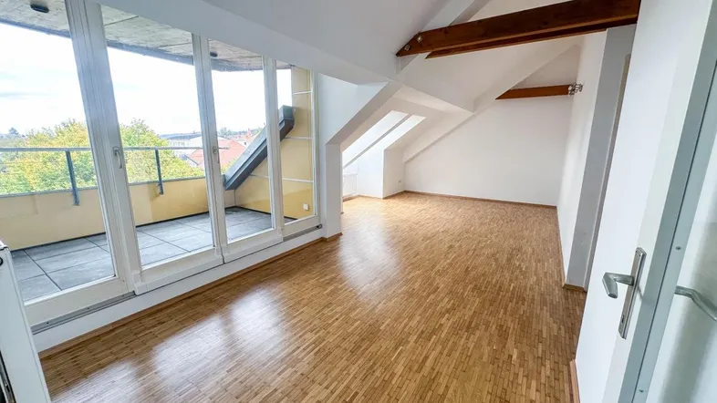 Helles Dachgeschosszimmer mit Holzboden, sichtbaren Balken und Zugang zu einem großen Balkon.