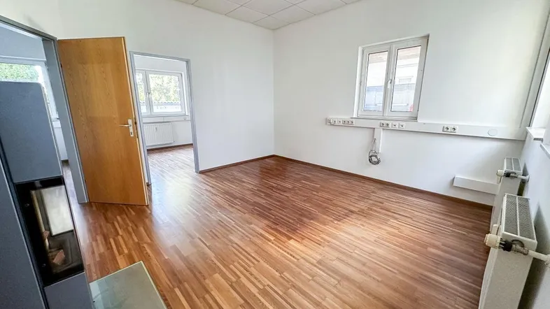 Geräumiges Büro mit hellem Holzfußboden, weißen Wänden und einem modernen Kaminofen.