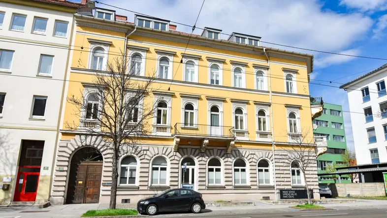 Gelbe Fassade eines historischen Gebäudes mit dekorativen Elementen und Balkon an einer Straße.