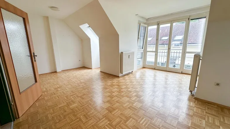 Geräumiges Zimmer im Dachgeschoss mit Parkettboden, Dachschrägen und Zugang zu einem französischen Balkon.
