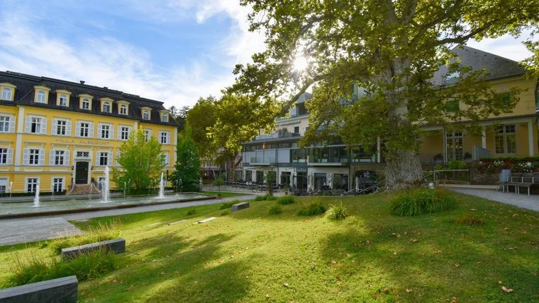 Historische gelbe Villa mit Springbrunnen und Grünflächen in sonniger Umgebung.