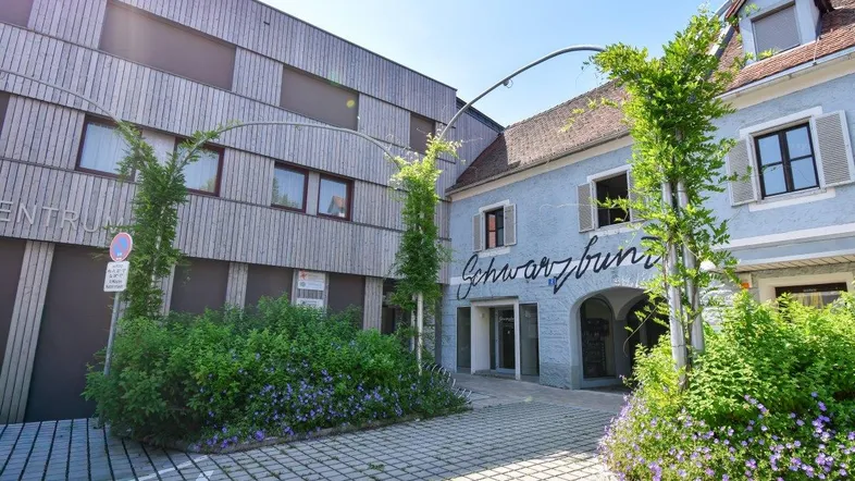 Ansicht der Gebäudefronten mit moderner Holzfassade und historischem Gebäude mit Schriftzug.