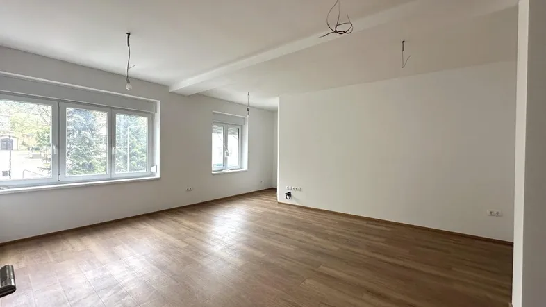 Helles, leeres Wohnzimmer mit Laminatboden und großen Fenstern, bereit zur individuellen Gestaltung.