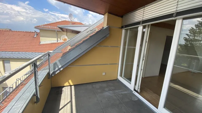 Geräumiger Balkon mit Fliesenboden und Blick auf die umliegenden Dächer und den Himmel.
