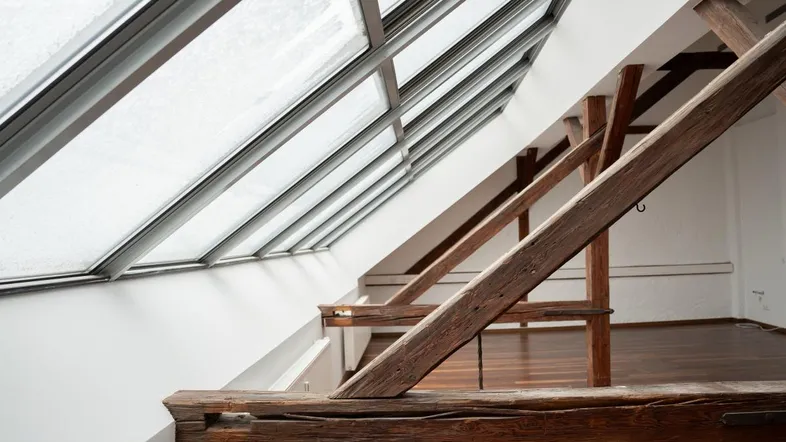 Heller Dachbodenraum mit großen Dachfenstern und sichtbaren Holzbalken, der viel natürliches Licht bietet.