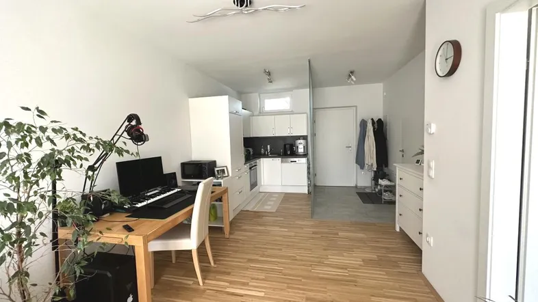 Helles, offenes Wohnzimmer mit Holzboden, Arbeitsbereich und integrierter Küchenzeile.
