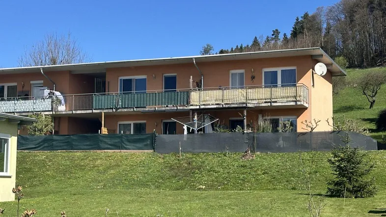 Mehrfamilienhaus mit mehreren Balkonen und grüner Umgebung am Hang, typisch für die 70er/80er Jahre.