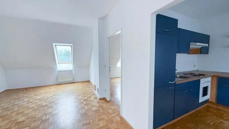 Heller Wohn- und Essbereich mit Parkettboden, Dachschrägen und integrierter Küchenzeile in Blau.