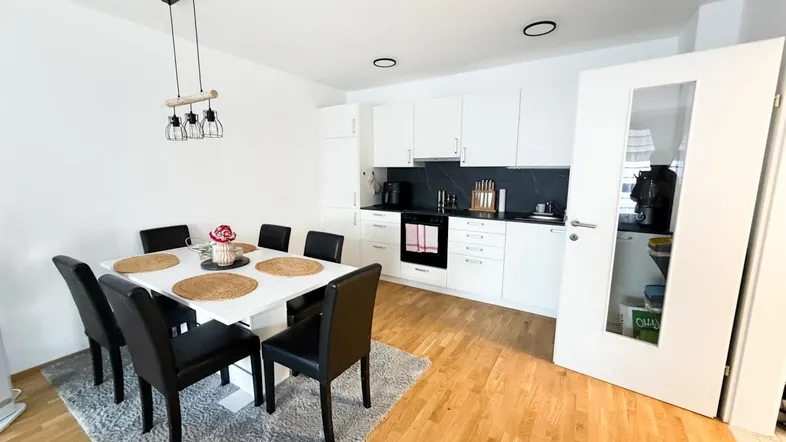 Moderne offene Küche mit Essbereich, weißen Schränken und Holzboden.