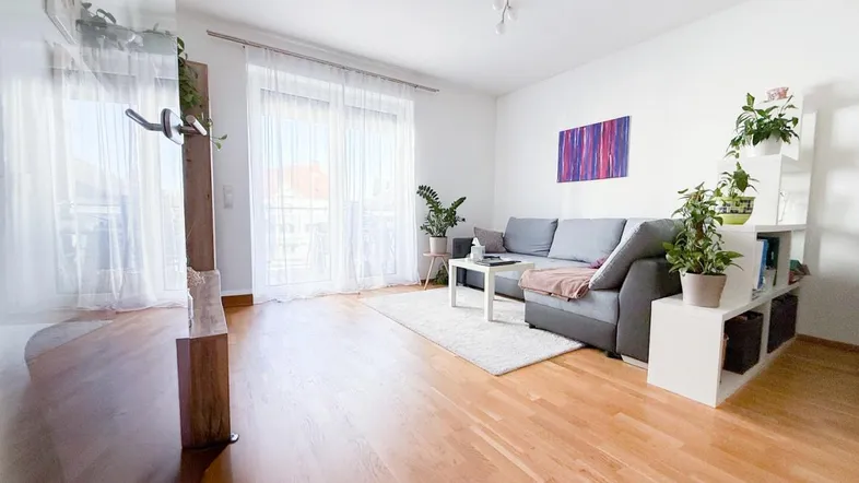 Helles Wohnzimmer mit Holzboden, gemütlichem Sofa und Zugang zu einem Balkon.