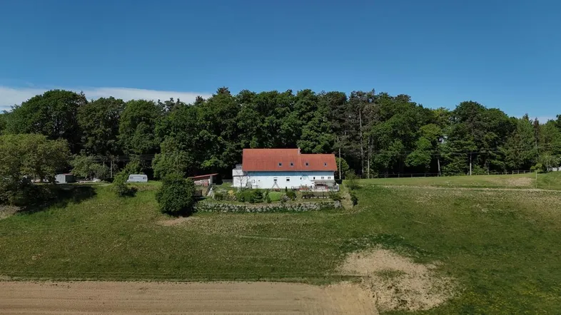 Freistehendes Haus mit rotem Ziegeldach und weißer Fassade, umgeben von Natur und Wald.