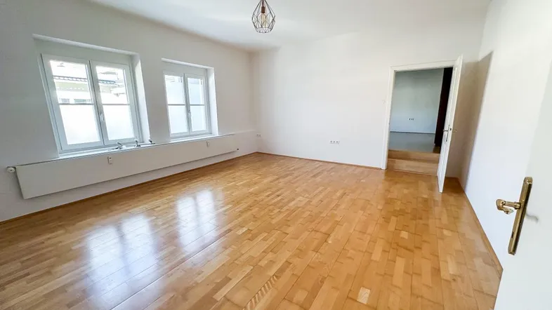 Helles, leeres Zimmer mit Parkettboden und zwei Fenstern, bereit zur individuellen Gestaltung.