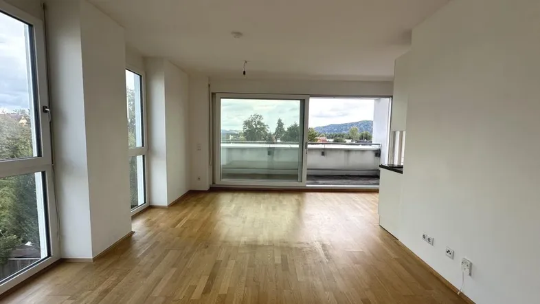 Helles Wohnzimmer mit Parkettboden, großen Fenstern und Zugang zu einem Balkon mit Weitblick.