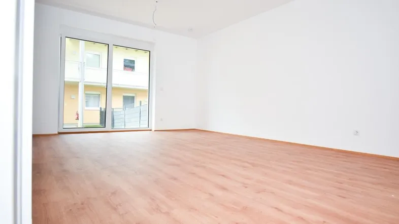 Heller, leerer Raum mit Laminatboden und großer Schiebetür zum Außenbereich.