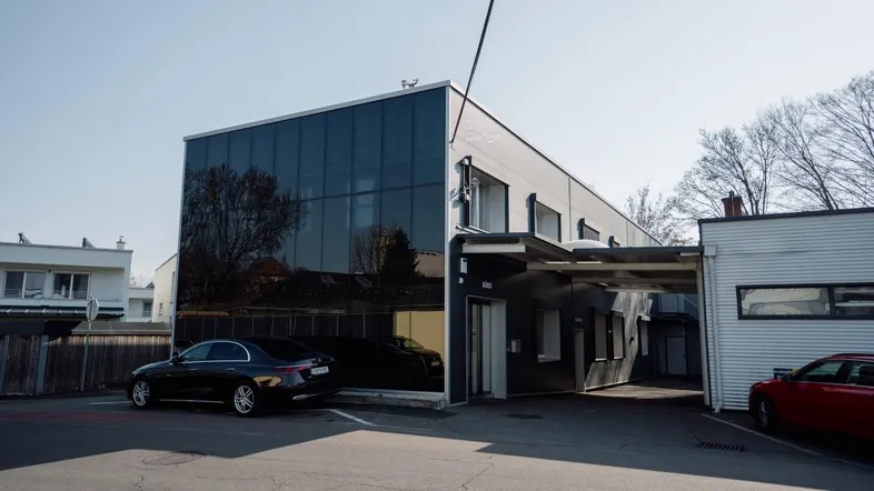 Modernes Geschäftsgebäude mit dunkler Glasfassade und Parkplätzen im Freien. Ein schwarzes Auto parkt davor.