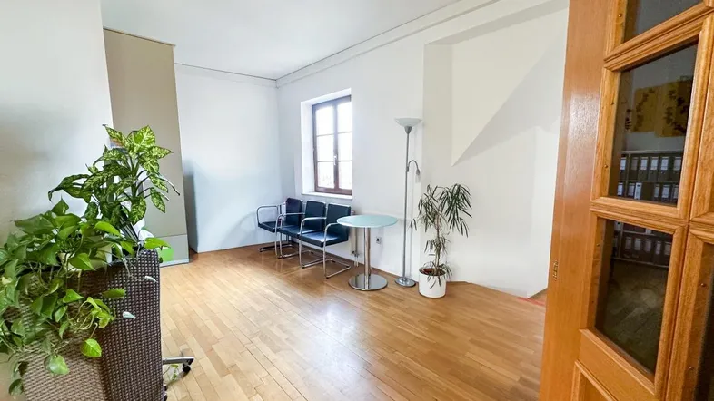 Heller Büroraum mit Holzfußboden, Wartebereich und Pflanzen, ideal für Empfang oder Besprechungen.