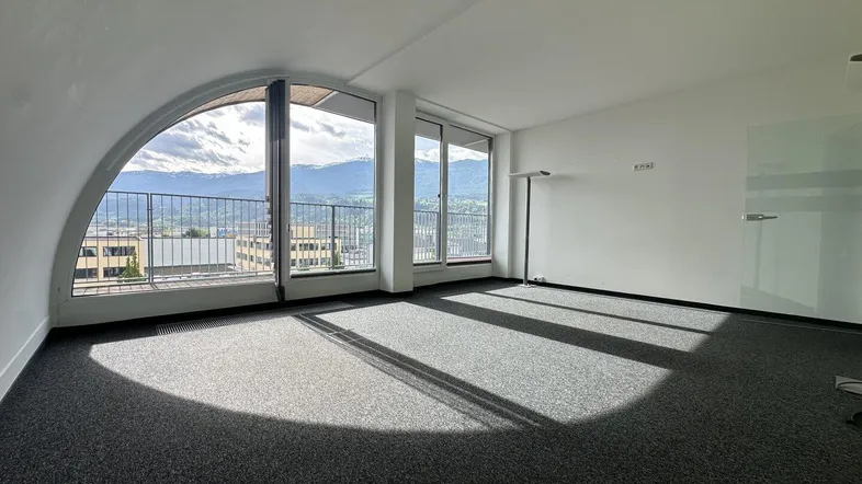 Geräumiger Büroraum mit großen Fenstern, die einen weiten Blick auf die Berge bieten und viel Tageslicht hereinlassen.