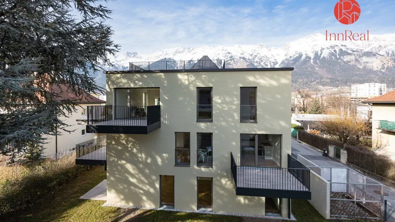 Modernes Mehrfamilienhaus mit Balkonen und beeindruckendem Bergblick in einer grünen Umgebung.