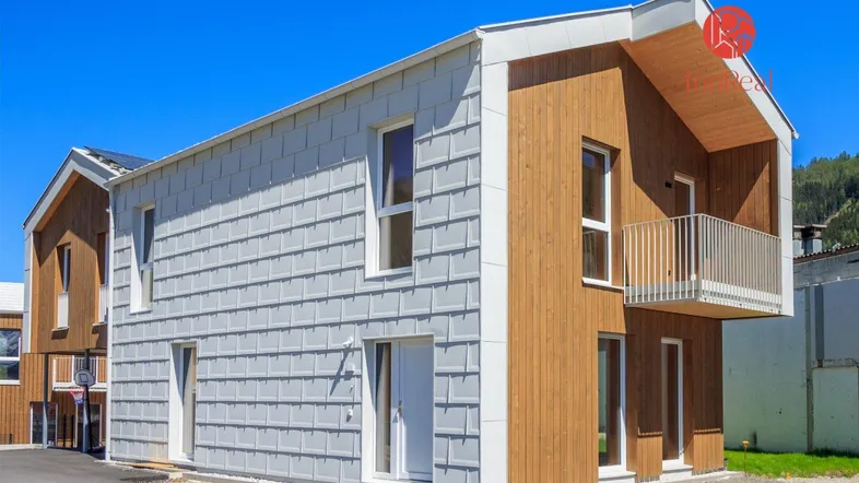 Modernes Einfamilienhaus mit Holz- und Schindelfassade unter blauem Himmel.