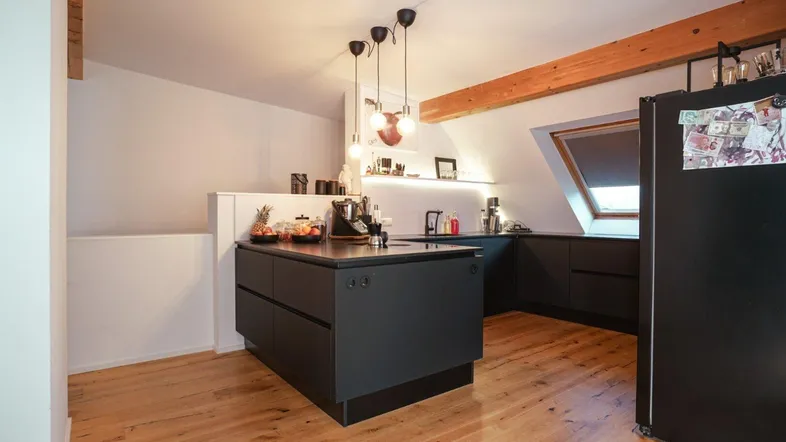 Moderne Küche mit schwarzer Kücheninsel, Holzboden, sichtbaren Holzbalken und Dachfenster.