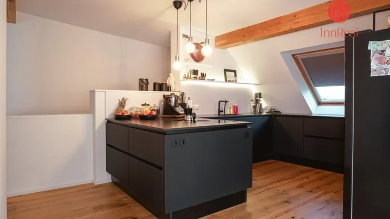 Moderne Küche mit schwarzer Kücheninsel, Holzboden, Dachschräge und sichtbaren Holzbalken.