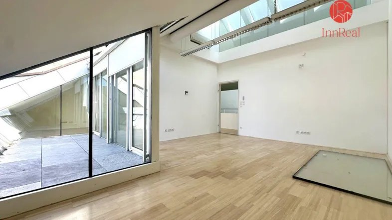 Heller, leerer Raum mit Holzparkett, großer Glasfront, Zugang zu einer Terrasse und Oberlichtern.