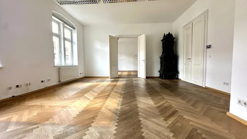 Geräumiger Raum mit Fischgrätparkett, hohen Decken und großen Fenstern, ideal für Wohn- oder Büronutzung.