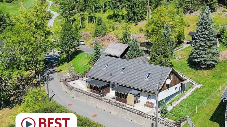 Luftaufnahme eines Hauses in einer grünen, bewaldeten Berglandschaft mit umliegenden Wegen.