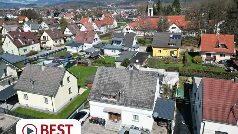 Luftaufnahme eines Wohngebiets mit Einfamilienhäusern und grüner Umgebung unter blauem Himmel.