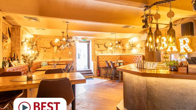 Gemütliche Bar mit rustikalem Ambiente, Holztischen, gepolsterten Bänken und Flaschenlampen, die eine warme Atmosphäre schaffen.