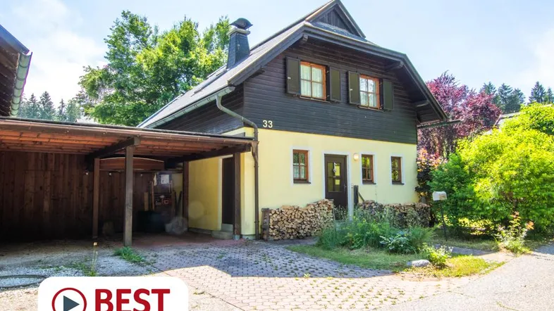 Traditionelles Haus mit Holzverkleidung, gelber Fassade und überdachtem Carport im Grünen.
