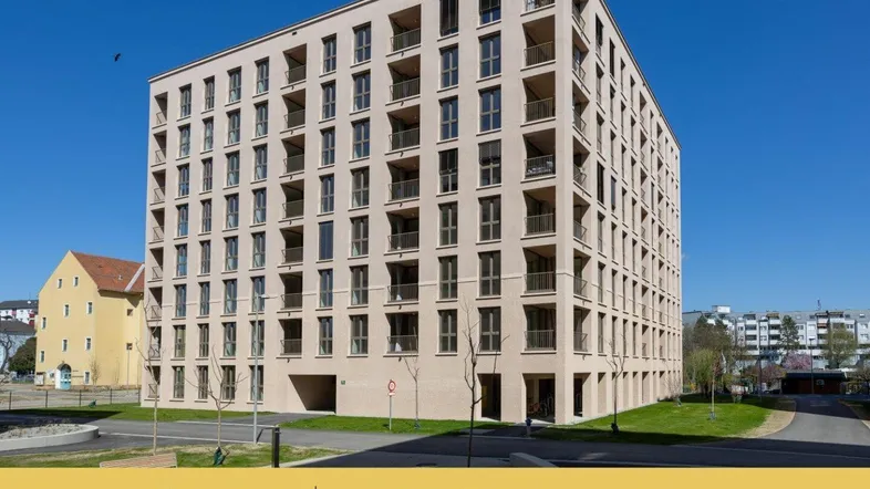 Modernes Mehrfamilienhaus mit zahlreichen Balkonen und heller Fassade unter blauem Himmel.
