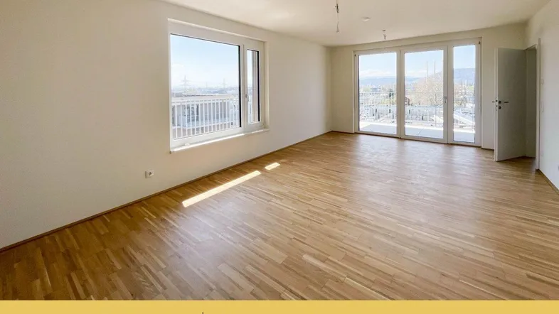 Helles Zimmer mit Parkettboden und Zugang zu einem Balkon, bietet viel Tageslicht.