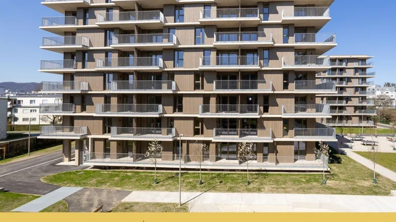 Modernes Mehrfamilienhaus mit vielen Balkonen und gepflegten Grünflächen in sonniger Umgebung.