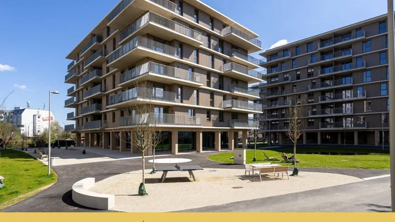 Moderne Wohngebäude mit Balkonen und begrünten Außenanlagen unter blauem Himmel.