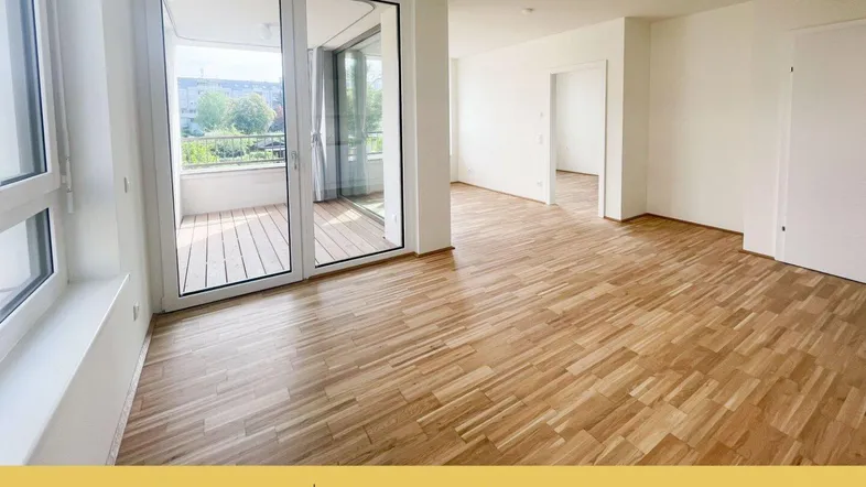 Helles Wohnzimmer mit Parkettboden und Zugang zu einem Balkon mit Blick ins Grüne.